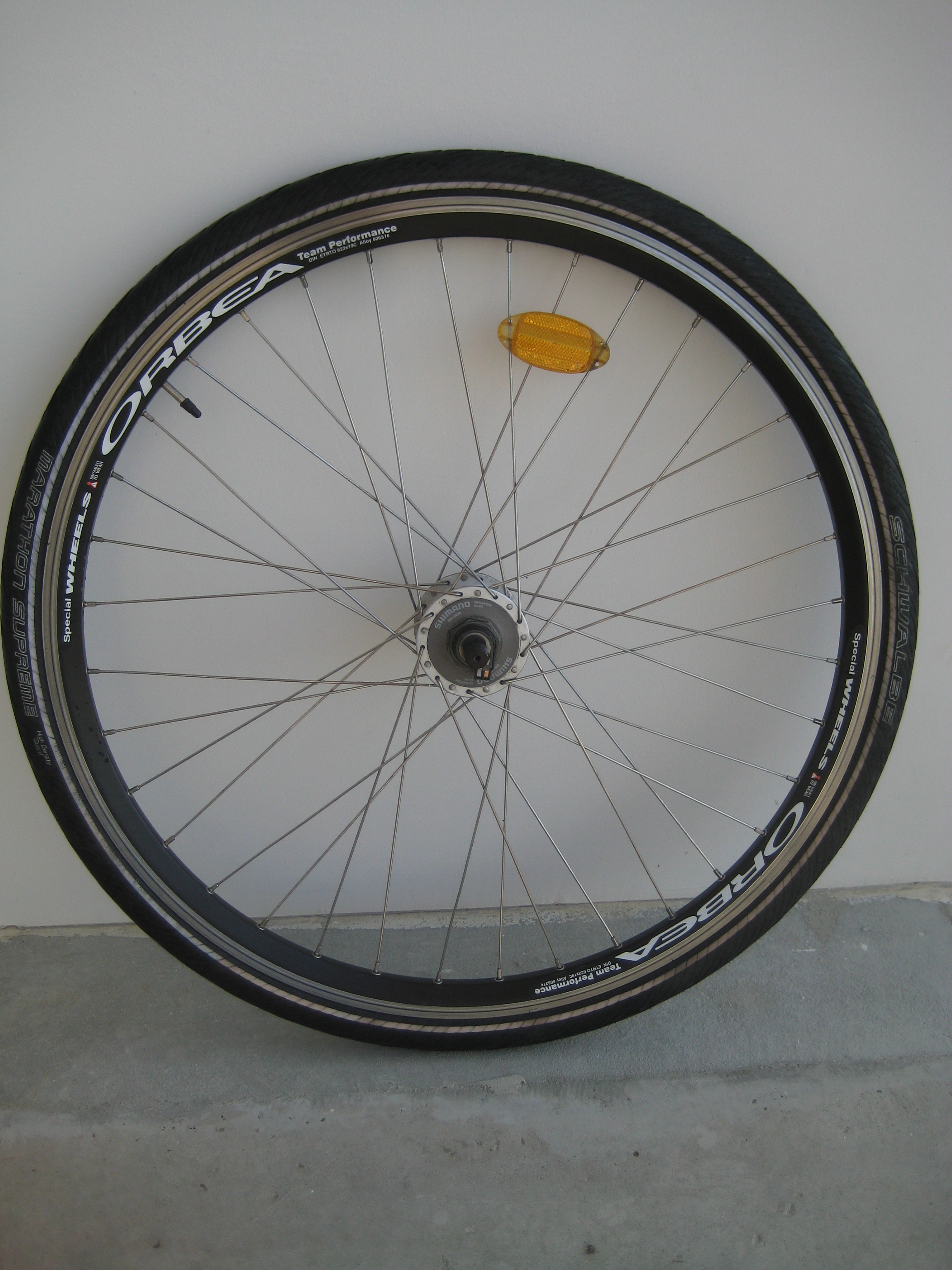 A loose trekking bicycle front wheel with a tire, rim-brake track, spokes, reflector, Schrader valve and dynamo hub